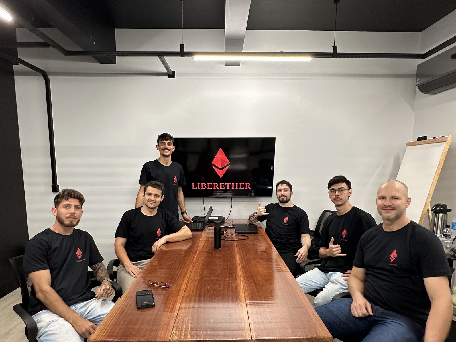 Encontro da comunidade LiberEther ao redor da mesa, com a marca na tela